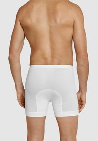 White cotton boxer briefs with a ribbed texture, featuring a fitted design and a logoed waistband. The back includes a reinforced panel.