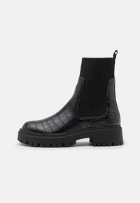 Botas negras de tobillo con un patrón de cocodrilo, una parte superior de tejido acanalado y una suela gruesa para mayor tracción.