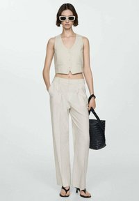 Top corto a rayas en color beige y pantalones de pierna ancha hechos de tejido ligero. La modelo lleva un bolso de mimbre negro y sandalias negras.