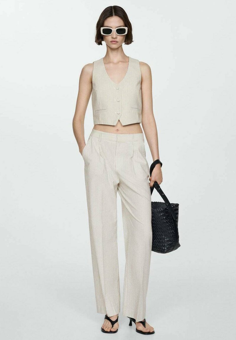 Top corto a rayas en color beige y pantalones de pierna ancha hechos de tejido ligero. La modelo lleva un bolso de mimbre negro y sandalias negras.