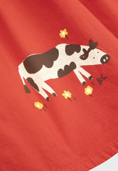 Tissu rouge avec une illustration en noir et blanc d'une vache entourée de fleurs jaunes et les lettres "I BC" près de ses pattes.