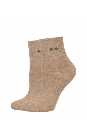 Coppia di calzini beige costine alla caviglia con marchio sottile vicino al bordo superiore su sfondo bianco.