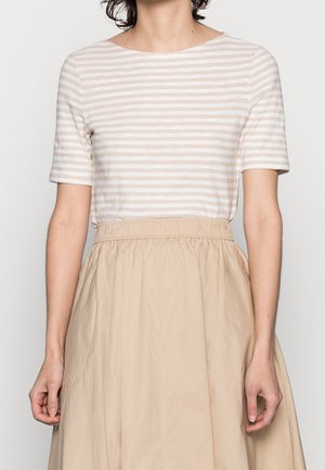 Vrouw draagt een beige-wit gestreept top met korte mouwen, ingestopt in een beige rokje met hoge taille en elastische tailleband.