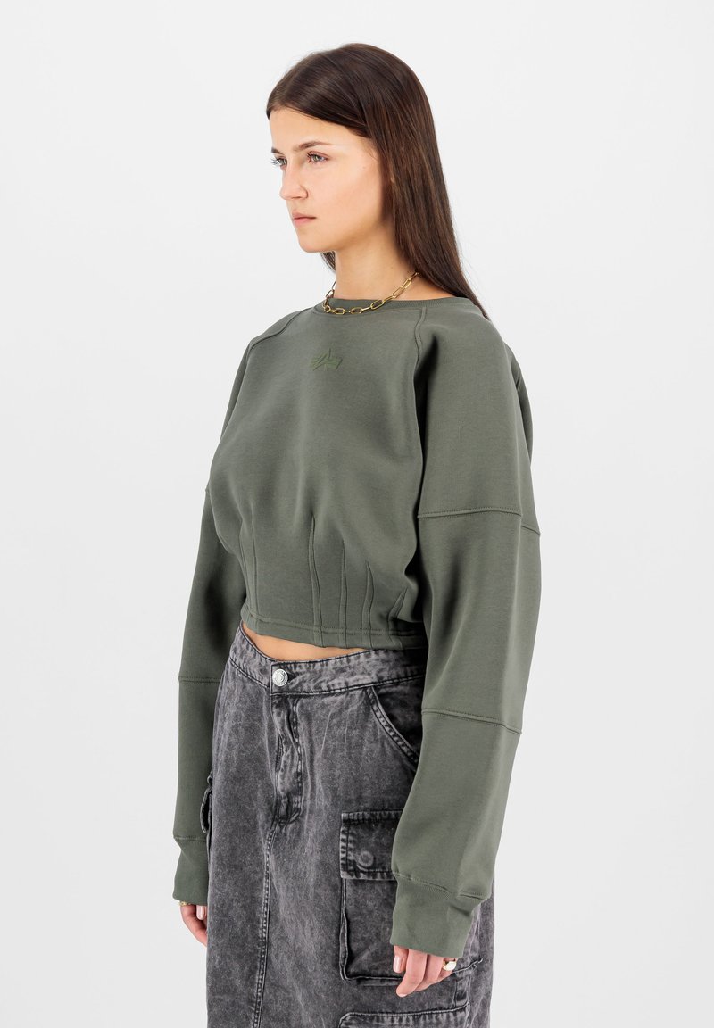 Rövidített, olívazöld pulóver bordás részletekkel és oversized ujjal, magas derékú, fakó fekete szoknyával, amely zsebekkel rendelkezik.