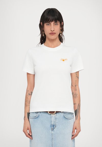 T-shirt en coton blanc avec un petit graphique de soleil orange, manches courtes et col rond. Texture lisse, design minimaliste.
