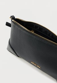 Sort tekstureret lædertaske med en guldlås og en flad bund. Har et logo på siden og en indvendig foret med glat materiale.