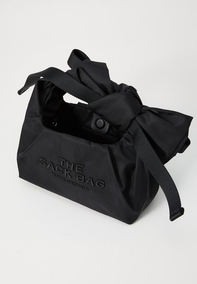 Bolsa de nylon negra con un asa superior anudada. Presenta el texto grabado "THE SACK BAG MARC JACOBS" en la parte frontal. Textura suave y forma estructurada.
