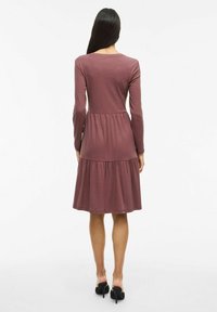 Långärmad, ribbad klänning i mauve med en figurnära bodice och en svängd, lager-på-lager kjol. Slät, lättviktig tyg med subtil textur.