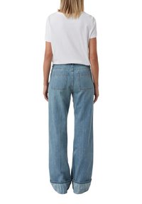 Jasnoniebieskie dżinsy o szerokich nogawkach z wysokim stanem, dwie tylne kieszenie i podwinięte mankiety, zestawione z prostym białym t-shirtem. Gładka tekstura denimu.