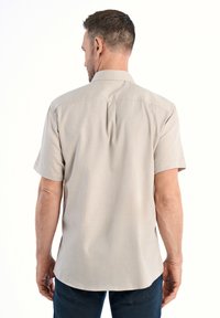 Camicia a maniche corte, color beige chiaro, con orlo dritto, dettaglio con piega sul retro e texture morbida. Il design presenta un colletto classico e chiusura con bottoni.
