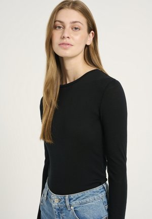 Black long-sleeve top in lightweight fabric, featuring a round neckline and a fitted silhouette, paired with high-waisted blue jeans.