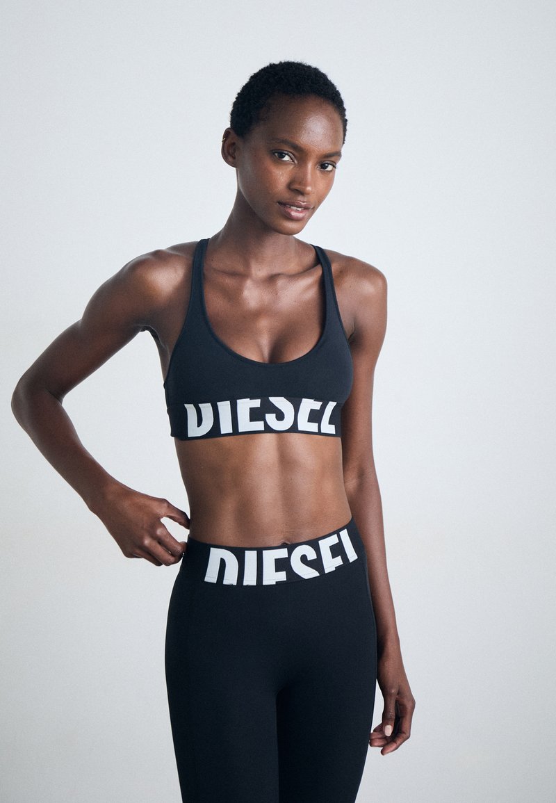 Juoda sportinė liemenėlė ir leggingai su baltu "DIESEL" logotipu. Pagaminta iš elastingos medžiagos, pasižyminti prigludusia forma ir lenkta nugaros dalimi.