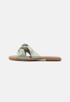 Satin grønne slidesandaler med et snoet stroppedesign og en flad, lysebrun sål. Glat tekstur med en minimalistisk stil.