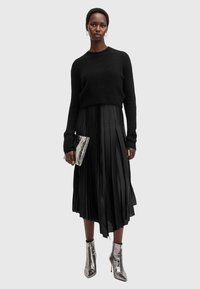 Schwarzer Strickpullover kombiniert mit einem plissierten schwarzen Midirock. Silberne metallische Ankle Boots und eine metallische Clutch. Gesamtmonochrom-Look.
