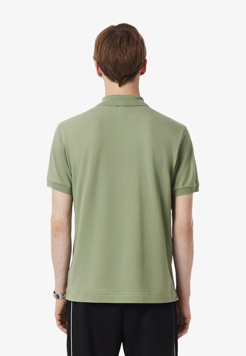 Polo shirt in soft olive green fabric, featuring a classic collar and short sleeves, with a straight hem and minimalistic design.