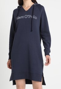 Vestido con capucha de color azul marino en material suave, con escote en V, mangas largas y aberturas laterales. Texto del logo "Marc O'Polo" en el frente.