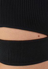 Svart ribbad tyg med ett utskuret mönster som visar hudton genom horisontella öppningar. Slät textur och åtsittande passform.