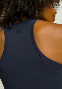 Top deportivo navy sin mangas con diseño de espalda nadadora, que cuenta con un pequeño logotipo en relieve en la parte trasera y una tela suave y elástica.