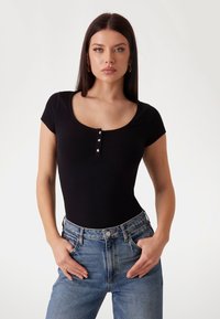 Svart ribbestrikket bodysuit med korte ermer og scoop-hals, med tre sølvfargede knappdetaljer foran.