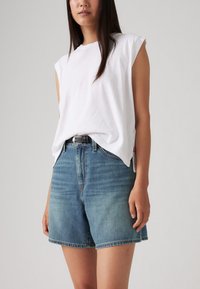 Vit bomullsskjorta utan ärmar tillsammans med ljusblå denimshorts. Shortsen har en avslappnad passform och rak skärning, och har en klassisk design med fem fickor.