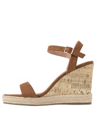 Bruine suède wedge sandaal met een kurkstructuur hak, verstelbaar enkelbandje en natuurlijke touwdetails rond de basis.