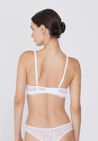Bralette en dentelle blanche avec des bretelles réglables, des bords festonnés et une fermeture à crochet au dos. Tissu doux et transparent avec des détails de motif floral.