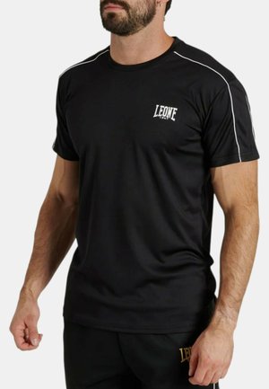 Uomo che indossa una maglietta sportiva nera a maniche corte e pantaloncini abbinati con piping bianco e logo "LEONE 1947" sul petto e sulla coscia.