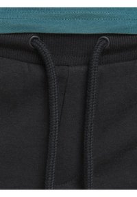 Gros plan de la ceinture d’un pantalon de survêtement gris foncé avec cordons noirs et une partie d’un t-shirt bleu sarcelle au-dessus.