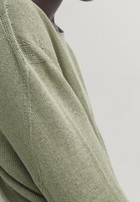 Light green knitted sweater with a textured finish and a relaxed fit, featuring subtle stitching details along the seams.