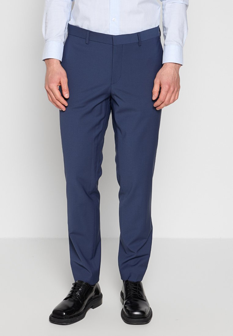 Pantaloni blu navy con una vestibilità slim, realizzati in un tessuto morbido con fronte piatto, tasche laterali e passanti per cintura, abbinati a scarpe nere.