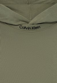 Oliva zöld kapucnis pulóver puha pamut keverék anyagból; kapucnival rendelkezik és a nyaknál fekete "Calvin Klein" logó található.