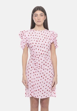 Donna con capelli lunghi e scuri che indossa un vestito rosa chiaro con macchie rosse, maniche corte a sbuffo e dettagli arricciati sul lato.