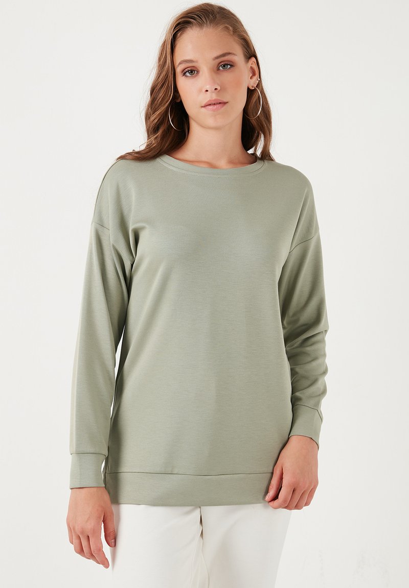 Camisa de manga larga en verde salvia apagado, hecha de tejido suave con un corte holgado, escote redondeado y puños acanalados.