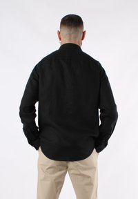 Camicia nera a maniche lunghe in lino, con colletto classico, taglio dritto e polsini con bottone, caratterizzata da una texture liscia e priva di fantasie.