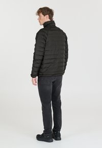 Giacca a vento nera con colletto alto, design trapuntato e maniche lunghe, abbinata a jeans scuri e calzature nere, vista da dietro.