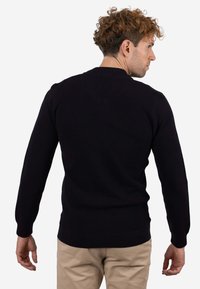 Suéter negro tejido con mangas largas y escote redondo, que presenta una tela texturizada y puños y borde acanalados.