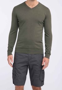 Olivgrüner V-Ausschnitt-Pullover aus Strickstoff, kombiniert mit dunkelgrauen Cargo-Shorts mit seitlichen Taschen und entspanntem Schnitt.