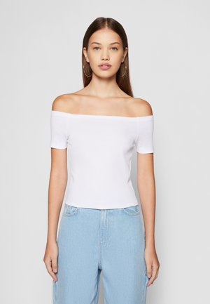 Weißes Off-Shoulder-Oberteil aus einem Baumwoll-Mischgewebe, mit kurzen Ärmeln und taillierter Passform, kombiniert mit hellblauen Jeans.