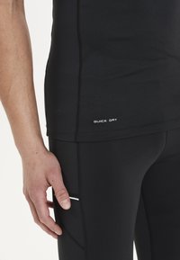 Schwarzes Sportshirt mit nahtlosem Design und "QUICK DRY"-Aufdruck. Verfügt über eine glatte Textur und einen figurbetonten Stil, kombiniert mit schwarzen Leggings.