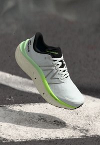 Bijela trkačka cipela s teksturiranim gornjištem, crnim detaljima i svijetlozelenim đonom s oznakom "Fresh Foam". Lagan i amortiziran dizajn.