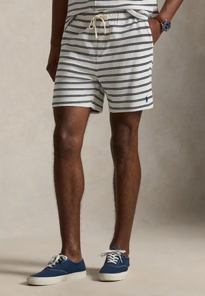 Ριγέ σορτς σε ναυτικό μπλε και κρέμ με ελαστική μέση και κορδόνι. Συνδυασμένο με μπλε αθλητικά παπούτσια με λευκά κορδόνια και σόλες.