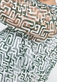 Haut en mesh transparent avec un motif géométrique vert et blanc, présentant une texture douce et une coupe ample, mettant en valeur des détails de conception complexes.