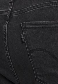 Černé džínové kalhoty s klasickým pětivreckovým designem, viditelným prošíváním a malou značkovou nášivkou na zadní kapse.