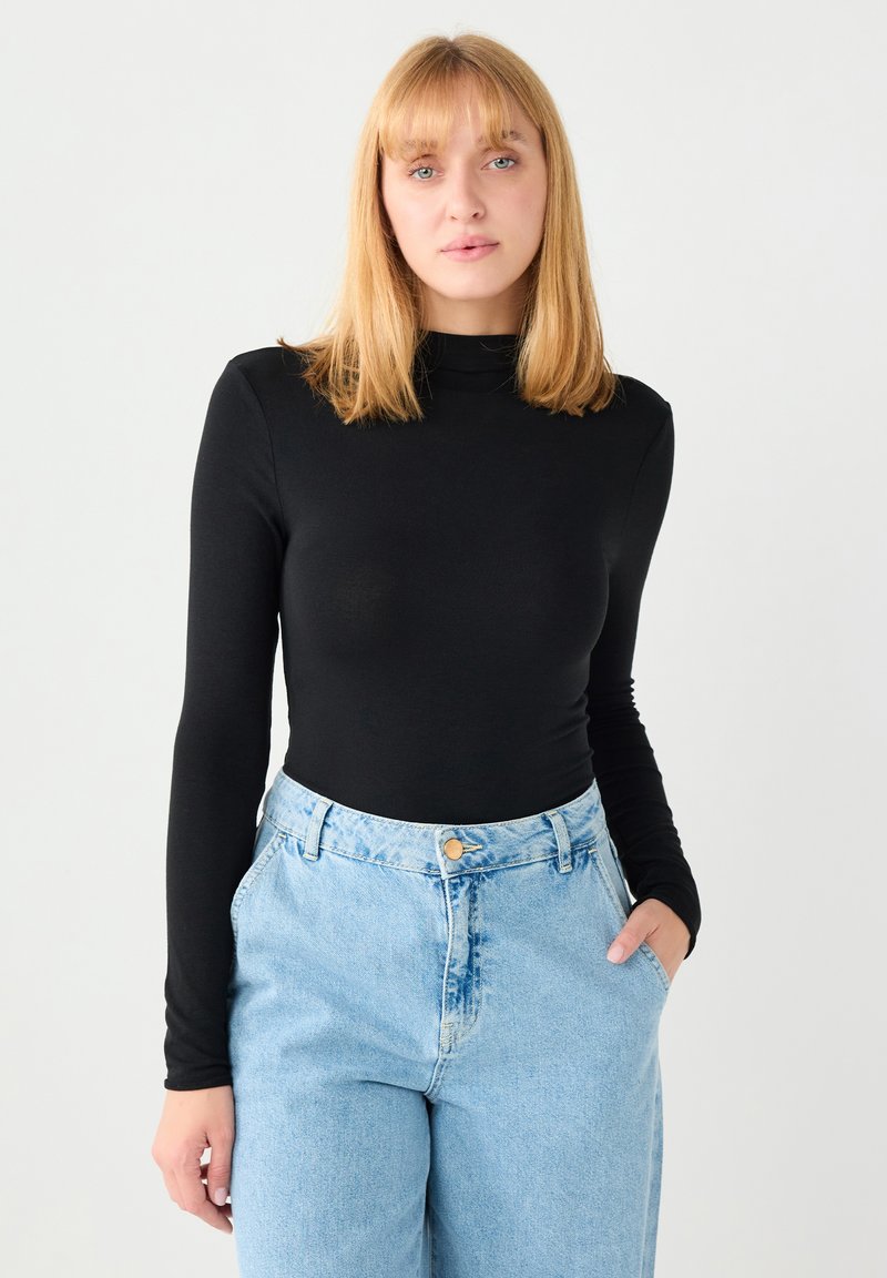Czarna bluzka z długim rękawem i wysokim kołnierzem w połączeniu z jasnoniebieskimi jeansami z wysokim stanem, wyposażonymi w zapięcie na guziki i boczne kieszenie.