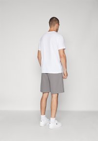 Camiseta de algodón blanca, pantalones cortos grises, zapatillas blancas con logo. Textura suave, corte casual, diseño sencillo y paleta de colores minimalista.