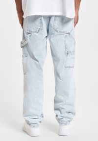 Lyseblå denim cargo bukser med en afslappet pasform, der har sidelommer og synlige sømdetaljer, parret med hvide sneakers.