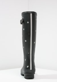 Botas de lluvia de goma negra con patrón de estrellas plateadas, raya vertical blanca, detalle de hebilla y suela texturizada para mayor agarre. Apto para condiciones húmedas.