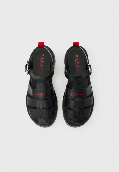 Μαύρα δερμάτινα ανδρικά σανδάλια με λουριά με αγκράφες, κόκκινες θηλιές στη φτέρνα και σήμανση "Marni" στις εσωτερικές σόλες και τα εμπρόσθια λουριά.