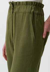 Olijfgroene broek gemaakt van een zachte stof, met een elastische tailleband, zijzakken en licht toelopende pijpen.