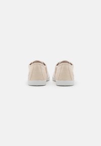 Scarpe slip-on in tela beige a righe, con suole in gomma bianca, caratterizzate da talloni arrotondati e tessuto texturizzato, progettate per comfort e facilità.